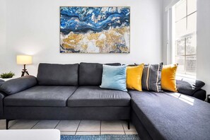 Uma sala de estar moderna com um sofá seccional cinza, um abajur e um grande quadro abstrato na parede.