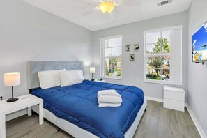 A bedroom with a bed, bedside tables, a ceiling fan, and large windows.