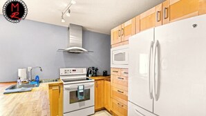 A modern kitchen with wooden cabinets, a white refrigerator, a built-in oven, a microwave, and a stainless steel sink.