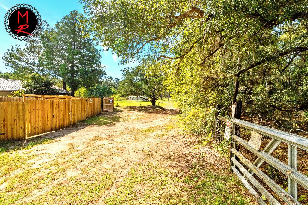 A dirt path leading to a wooden gate in a rural setting with trees and a fence.