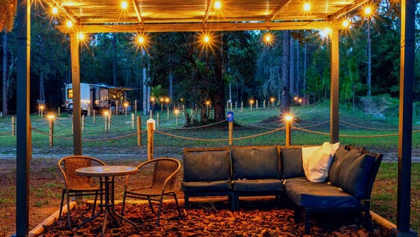 A covered seating area with a bench and chairs, surrounded by a rope barrier, and string lights overhead.