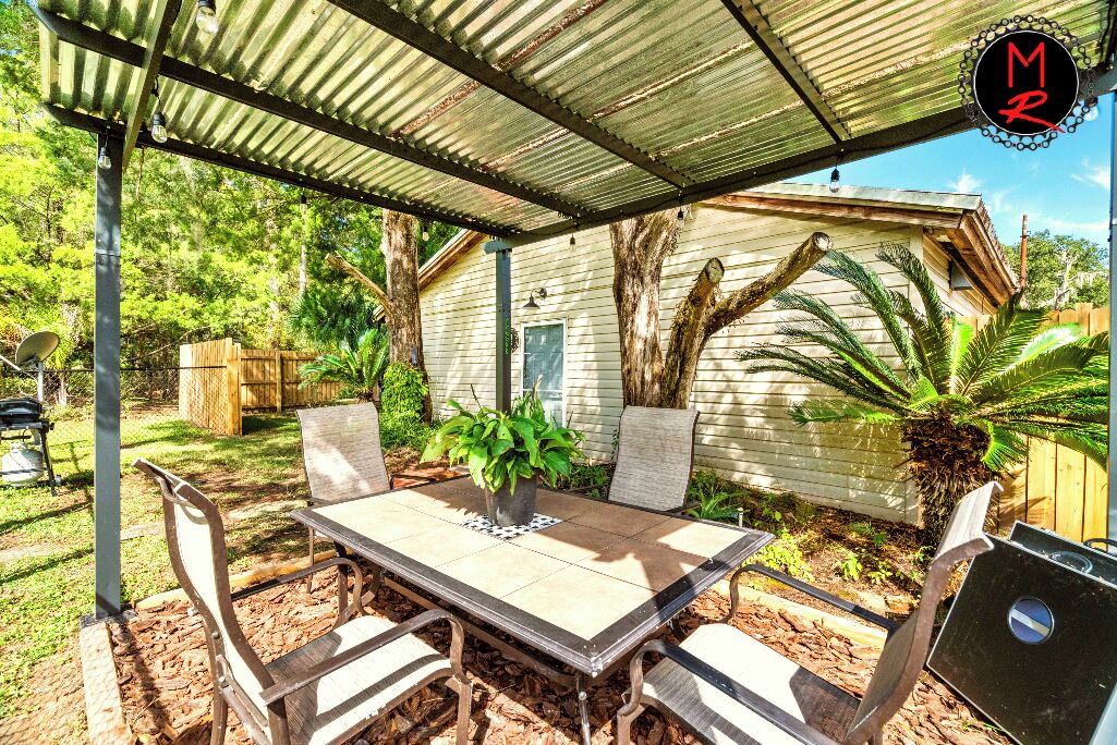 Un patio al aire libre con una mesa y sillas, rodeado de árboles y una valla de madera.