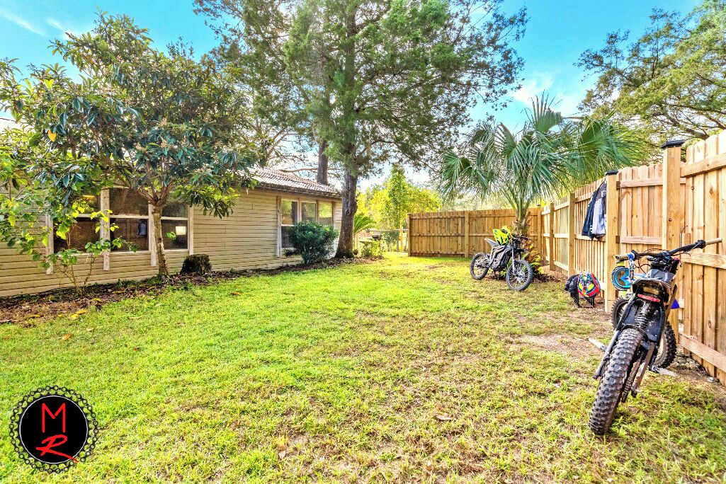 A backyard with a wooden house, a dirt bike, and a fence.