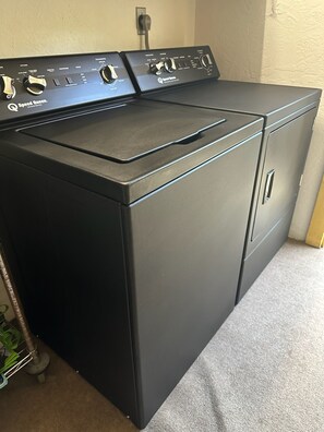 A black front-loading washer and dryer unit with control knobs and a power cord plugged in.