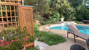 A pool area with a wooden fence, lounge chairs, and a variety of plants.