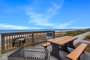 Una terraza de madera con mesas de picnic y una parrilla, con vista a la playa.