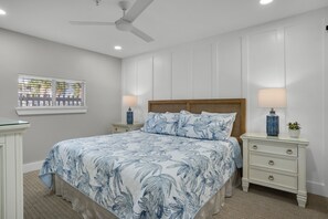 Un dormitorio con cama, mesitas de noche, ventana y ventilador de techo.