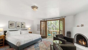 A bedroom with a bed, bedside tables, a sofa, a fireplace, and a balcony with chairs.