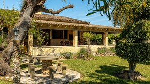 A traditional Mediterranean-style building with a patio, stone table, and surrounding greenery.