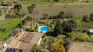 An aerial view of a residential area with a swimming pool, surrounded by greenery and a few buildings.