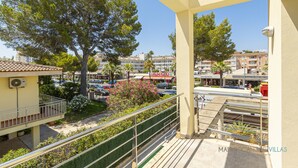 A balcony with a view of a parking lot, trees, and buildings in the background. - Villa Albufera en Playa Muro by Mallorca North Villas (Platja de Muro)