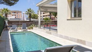 A swimming pool with lounge chairs, a covered seating area, and a view of the surrounding buildings. - Villa Albufera en Playa Muro by Mallorca North Villas (Platja de Muro)