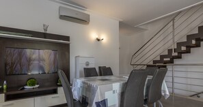 Un espace repas moderne avec une table dressée pour quatre personnes, un climatiseur intégré et un escalier doté d’une rampe en métal.