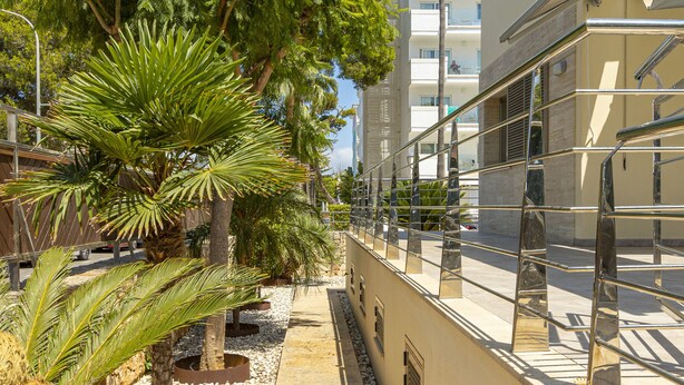 A modern building with a metal railing and palm trees. - Villa Albufera en Playa Muro by Mallorca North Villas (Platja de Muro)