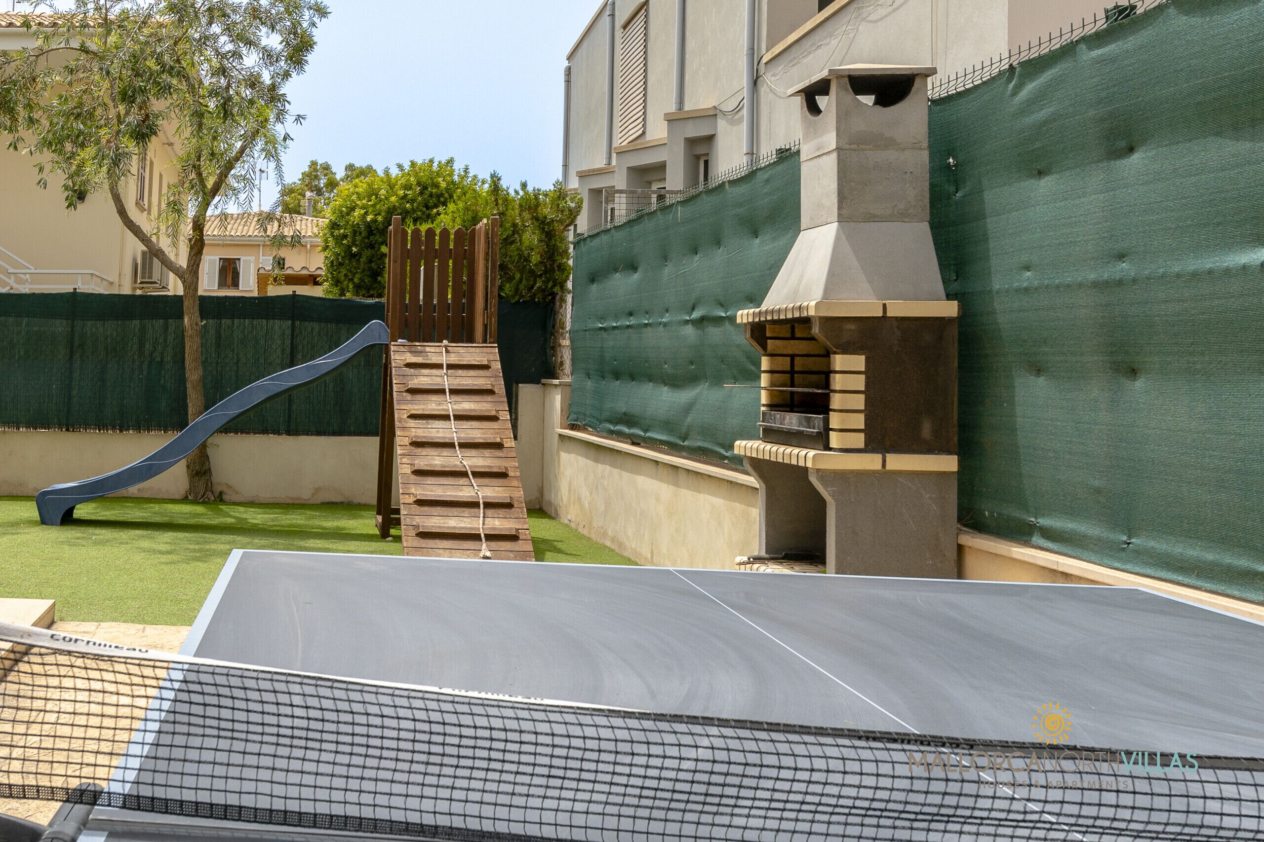 Un giardino con uno scivolo, un'area barbecue e un campo da tennis.