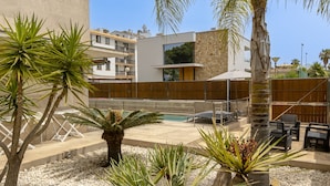 Un área de piscina moderna al aire libre con palmeras y un muro de piedra.