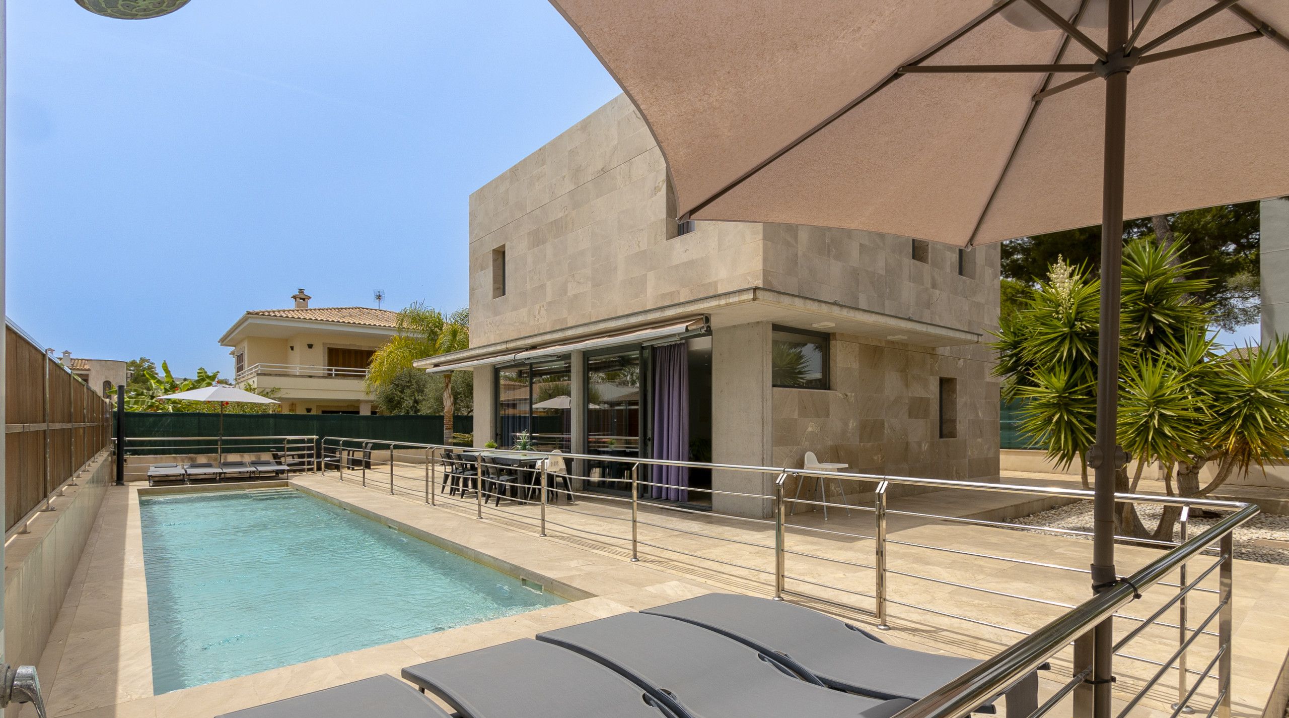 Ein Schwimmbecken mit Liegestühlen, einer überdachten Lounge und einem Gebäude im modernen Stil.