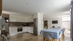Et moderne køkken med hvide skabe, et stålkøleskab og et spiseområde med et bord dækket af en mønstret dug.