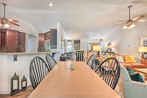 Un salón amplio con una gran mesa de madera para comer, asientos cómodos y un ventilador de techo.