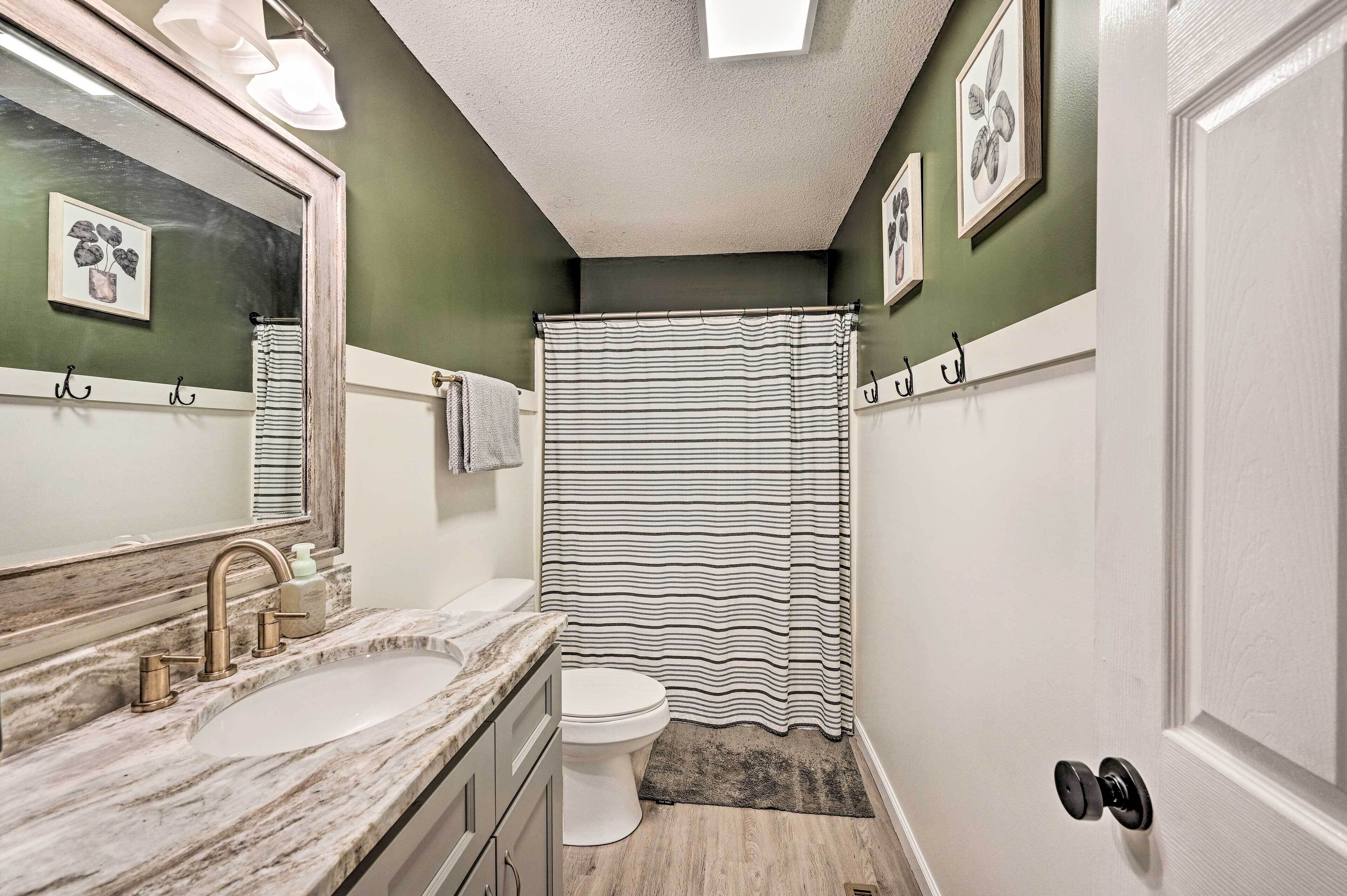 A bathroom with a marble sink, a toilet, a striped shower curtain, and a mirror with a plant decoration.
