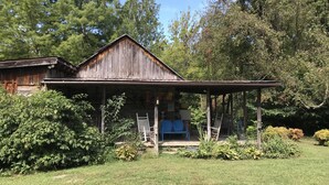 A rustic wooden building with a porch, surrounded by lush greenery and trees. - Peacocks, blacksmithing, buffalo, wildlife, a studio cabin by the pond. (Unicoi)