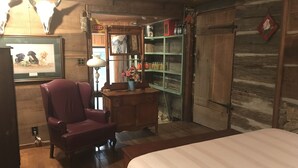 A rustic room with wooden walls, a wooden bed, a red armchair, a dresser, a mirror, and shelves with jars and baskets. - Peacocks, blacksmithing, buffalo, wildlife, a studio cabin by the pond. (Unicoi)