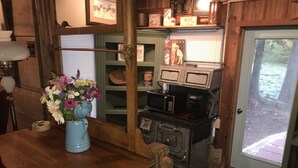 A rustic kitchen with a vintage stove, a microwave, and a vase of flowers on the counter. - Peacocks, blacksmithing, buffalo, wildlife, a studio cabin by the pond. (Unicoi)