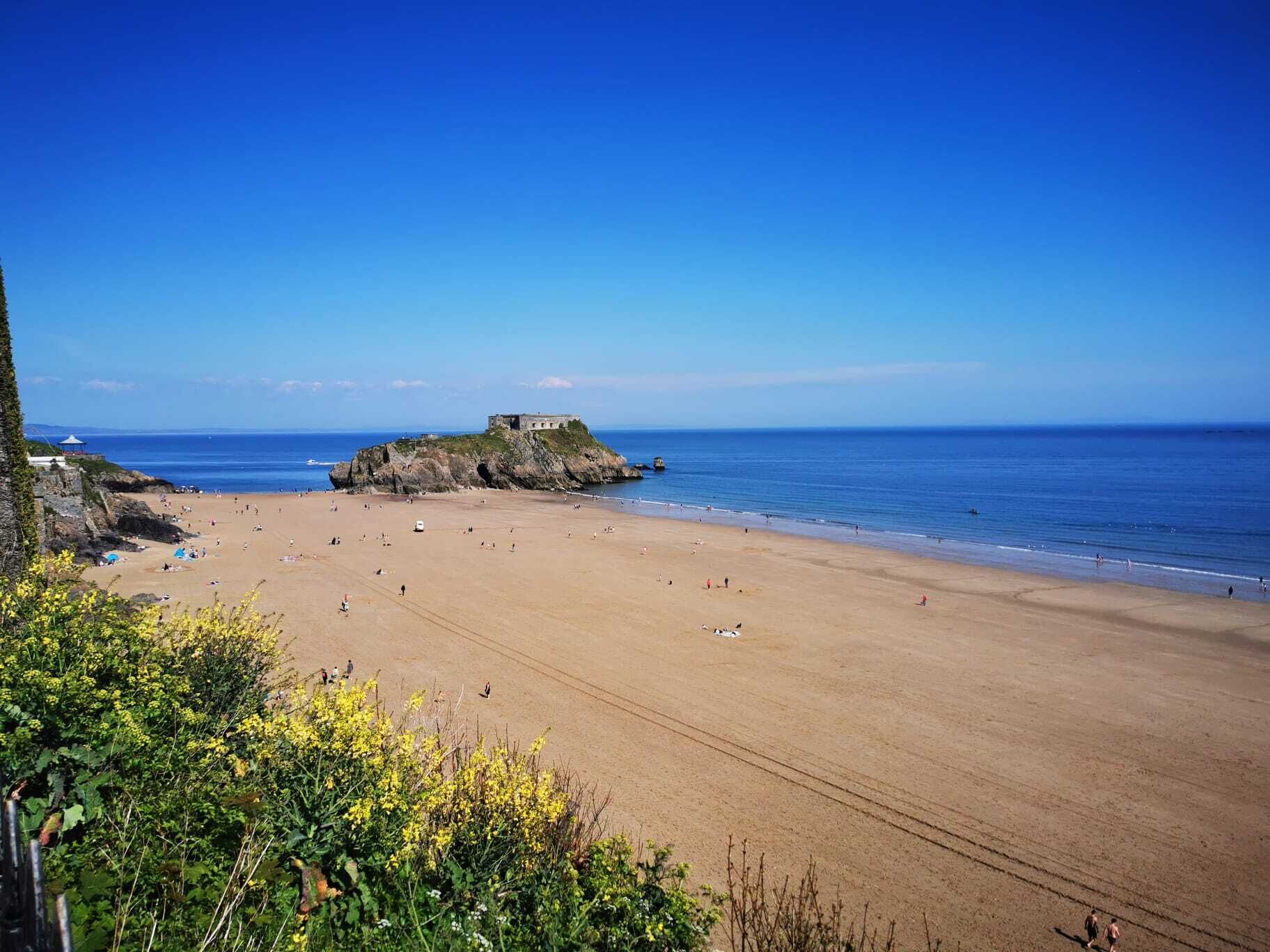 A beach with a rocky outcrop and a building on top.
