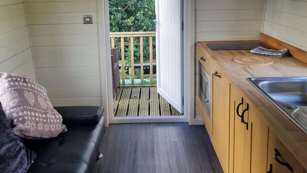 Een compacte keuken met een houten aanrechtblad en een inbouwoven. Een schuifdeur leidt naar een terras met een houten balustrade.