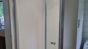 Een douchecel met glazen wanden, een witte betegelde vloer en een zichtbare douchekop.