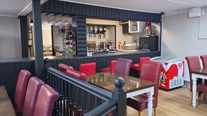 A restaurant with a bar area, red upholstered chairs, a table with a white tablecloth, and a popcorn machine.