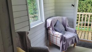 A corner room with a chair and a table, a window, and a view of greenery outside.