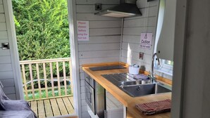 A compact kitchen with a wooden countertop, stainless steel sink, and a caution sign for hot water.