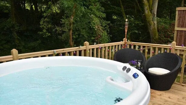 Een hottub op een houten terras met een houten reling en rieten stoelen.