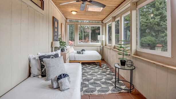 A cozy room with a ceiling fan, two beds, a small table, and large windows. - Sedona Mountain Trail: A 2BR luxury home in West Sedona with stunning red rock views. (Sedona)