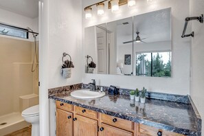 A bathroom with a marble countertop, wooden cabinets, a large mirror, and a shower. - Sedona Mountain Trail: A 2BR luxury home in West Sedona with stunning red rock views. (Sedona)