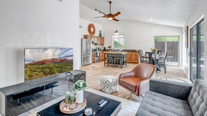 A modern living room with a flat-screen TV, a coffee table with decorative items, a leather armchair, and a gray sofa. - Sedona Mountain Trail: A 2BR luxury home in West Sedona with stunning red rock views. (Sedona)