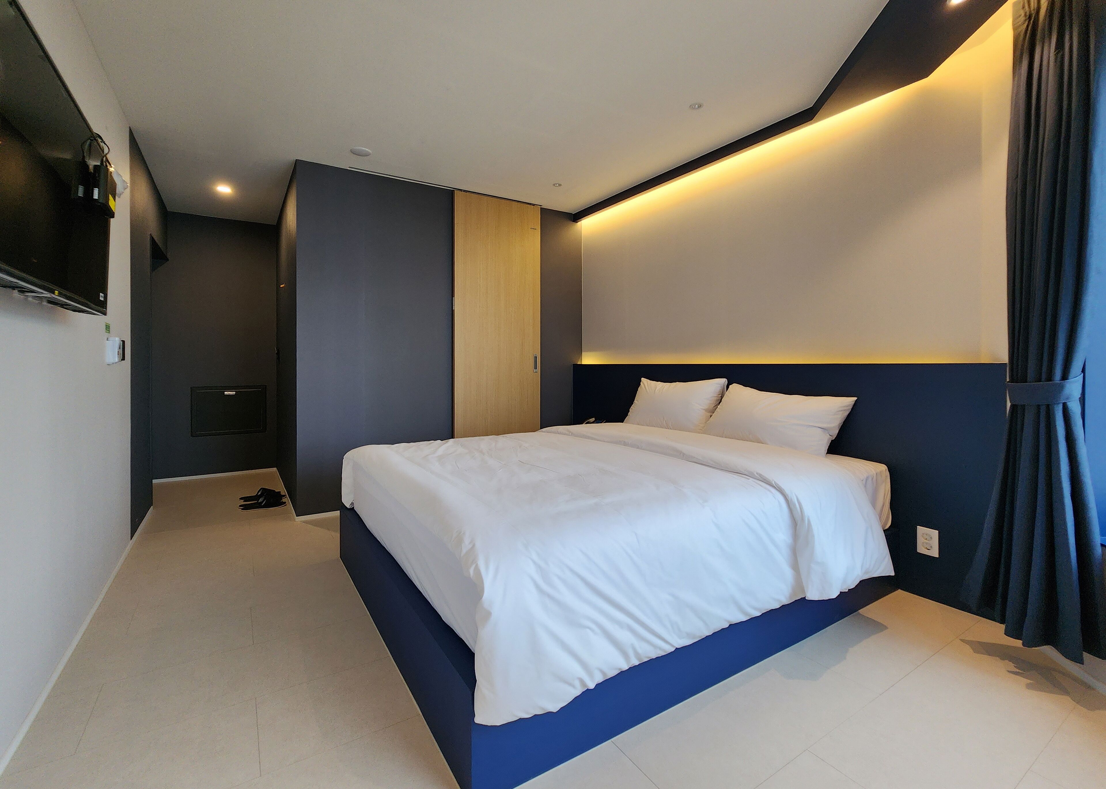 Una habitación de hotel moderna con una cama grande, un televisor de pantalla plana montado en la pared y una mesita de noche.