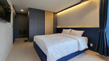 Una habitación de hotel moderna con una cama grande, un televisor de pantalla plana montado en la pared y una mesita de noche.
