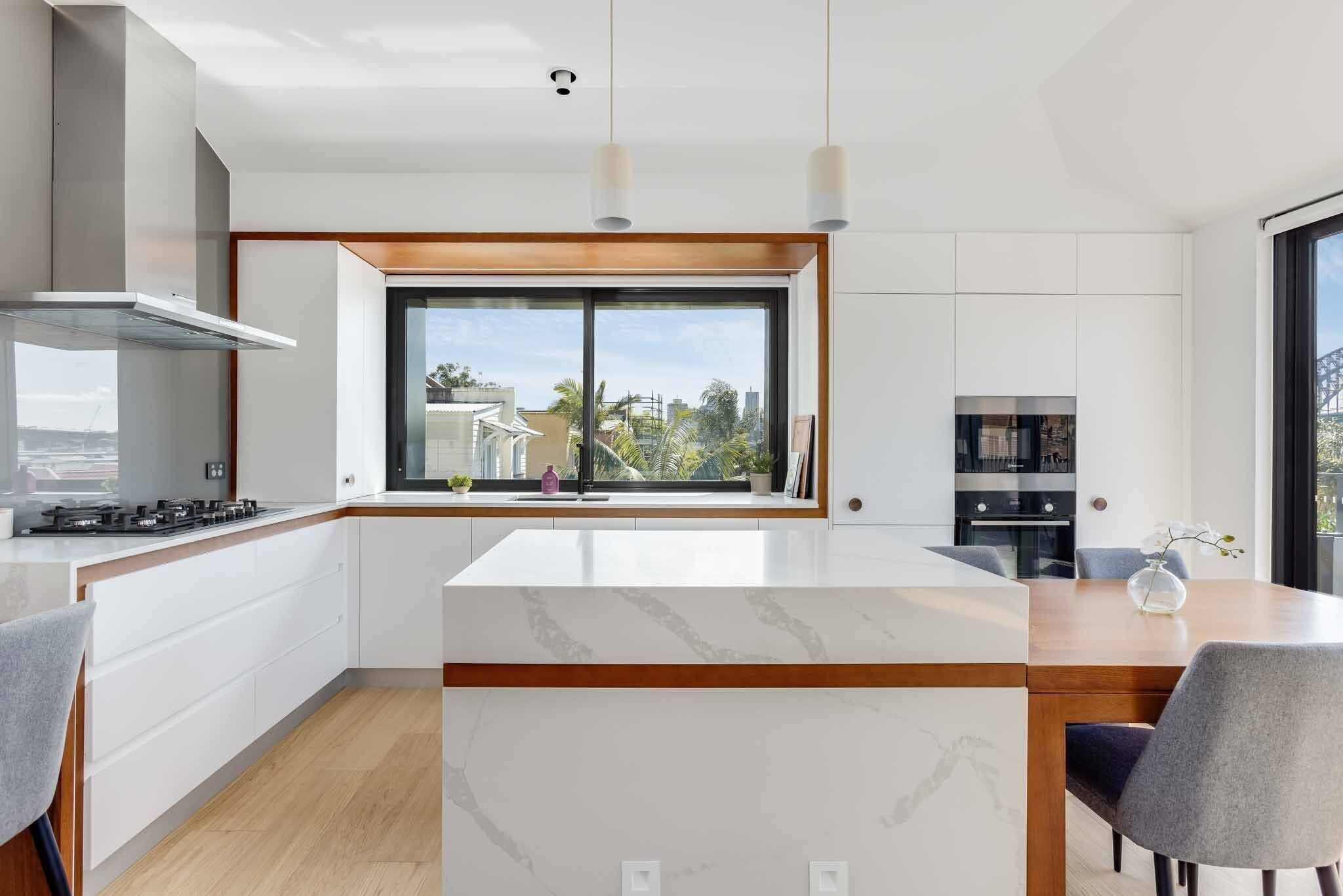 A modern kitchen with a large window, white cabinetry, and a marble countertop.