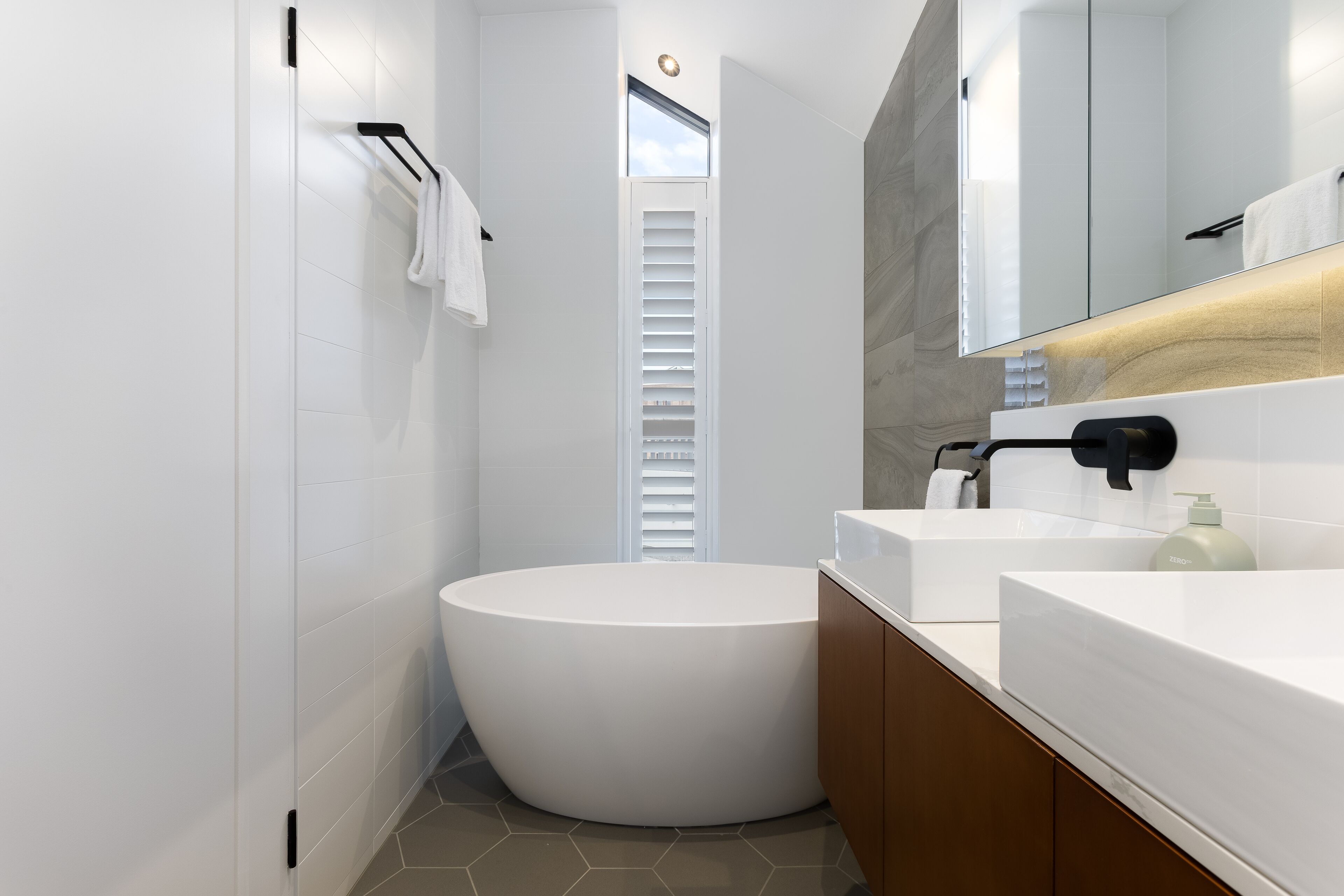 A modern bathroom with a freestanding bathtub, a large mirror, and a white vanity with a soap dispenser.