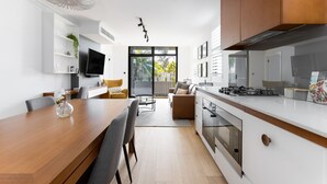 Une cuisine moderne avec des meubles blancs, une table à manger en bois et un four encastré.