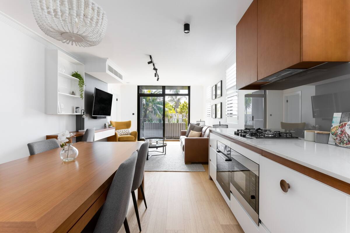 A modern kitchen with white cabinets, a wooden dining table, and a built-in oven.