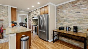 Una cocina con refrigerador de acero inoxidable, armarios de madera, encimera de granito y pared de ladrillo.