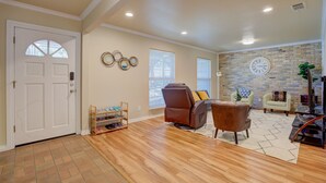 Amplia sala de estar con piso de madera, un sofá de cuero marrón, un sillón blanco y una pared de ladrillo decorativa.