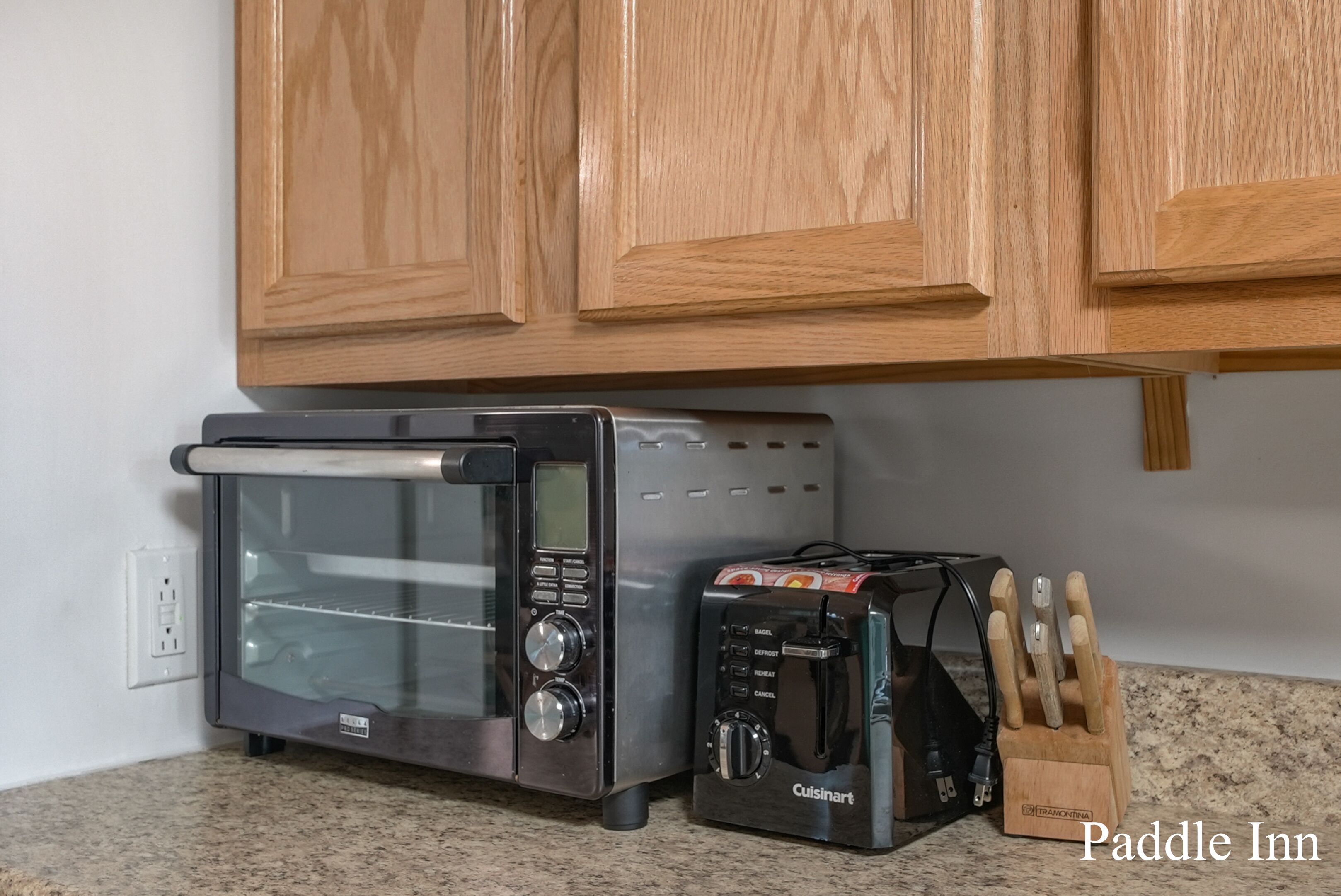 A kitchen with a toaster oven, a bread toaster, and a knife block on the counter.
