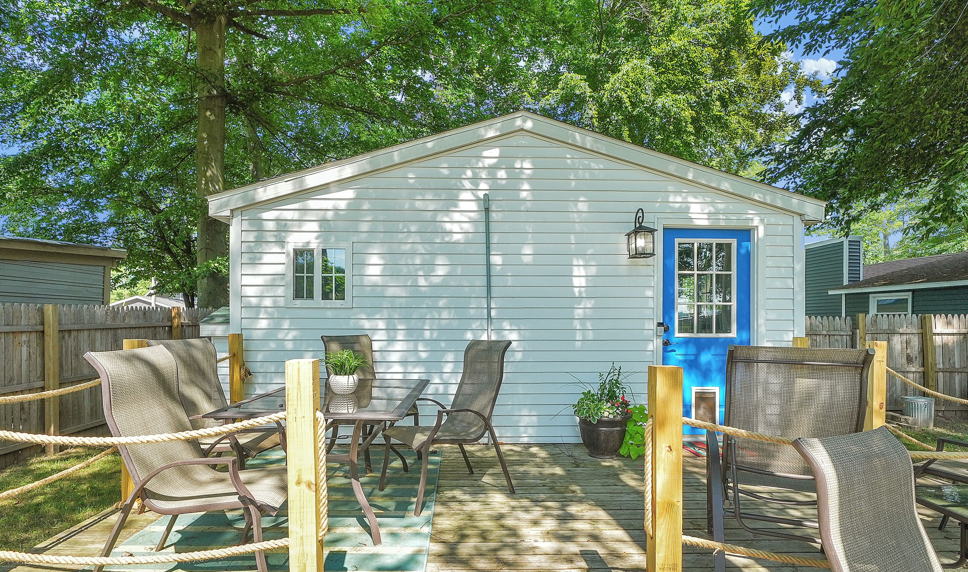 A small white building with a blue door, surrounded by wicker chairs and a wooden deck.