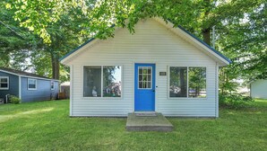 Ein kleines, eingeschossiges Haus mit blauer Tür und Fenstern, umgeben von Gras und Bäumen.