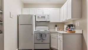 A compact kitchen with white cabinetry, a built-in oven, a microwave, and a refrigerator. - Spacious one-bedroom beach apartment on Singer Island (Palm Beach Shores)