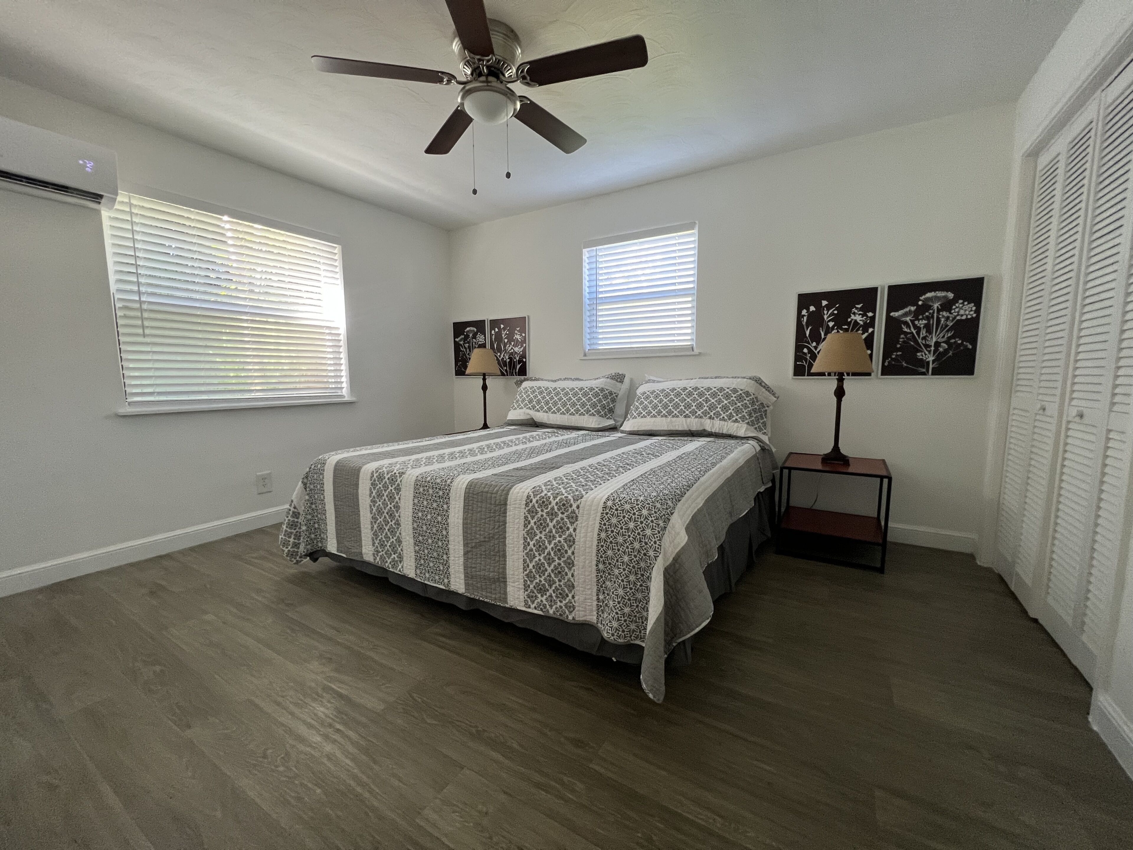 A bedroom with a bed, two bedside tables, a ceiling fan, and two windows with blinds.